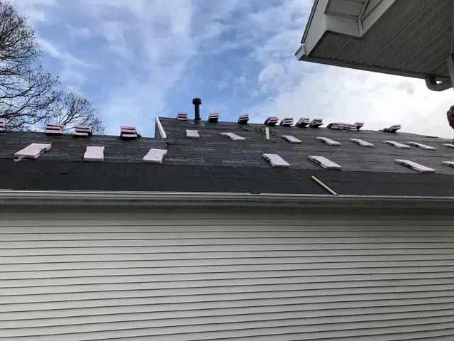 House roof with pink foam insulation pieces; blue sky background.