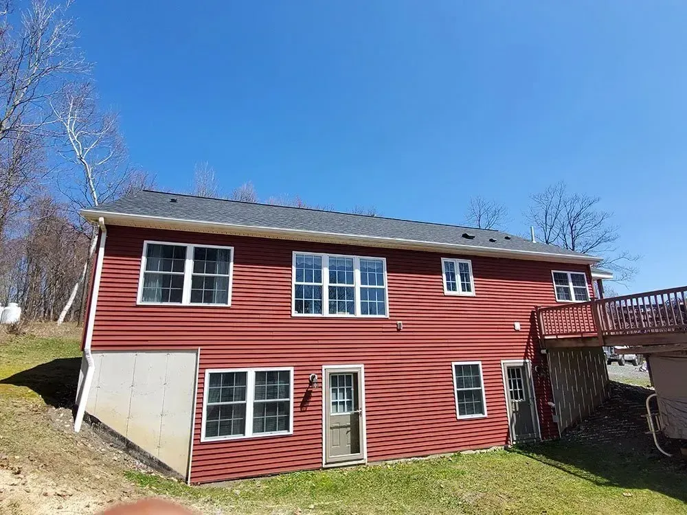 Red-sided two-story house with multiple windows, a door, and a deck, set against a blue sky.