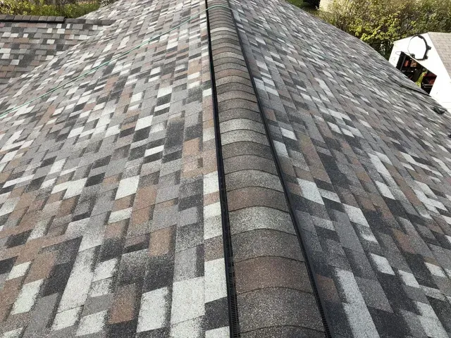 Close-up of a roof with a ridge, covered in brown, gray, and black asphalt shingles.