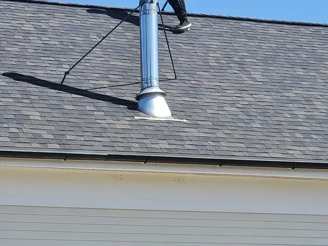 Person standing on a roof, near a silver chimney, on a sunny day.