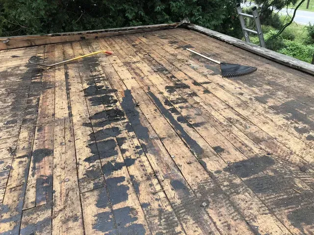 Damaged wooden roof with dark staining, measuring tape, and debris.