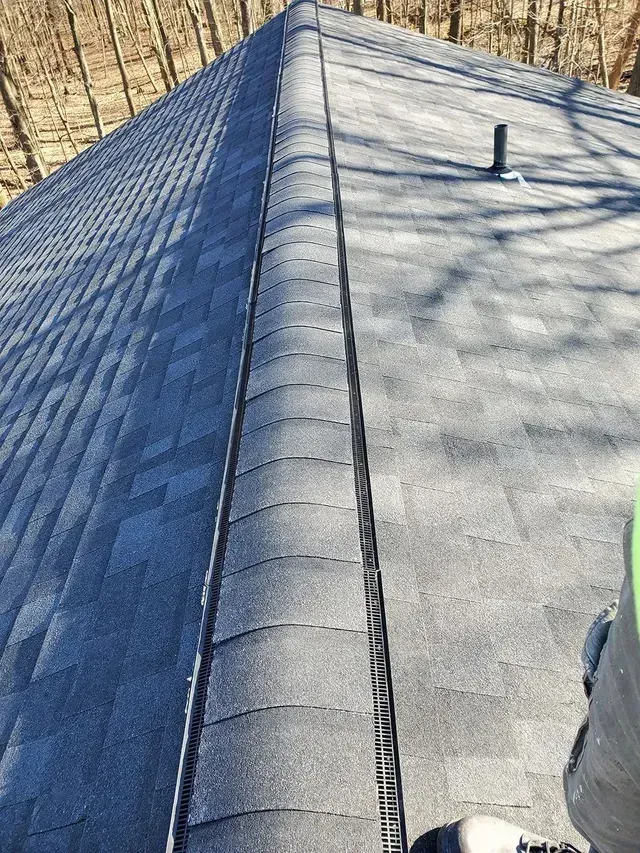 Dark gray shingled roof with a black metal valley. A pipe vent is visible.
