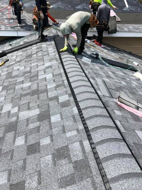 Roofers installing shingles on a gray roof, focusing on a black ridge cap.