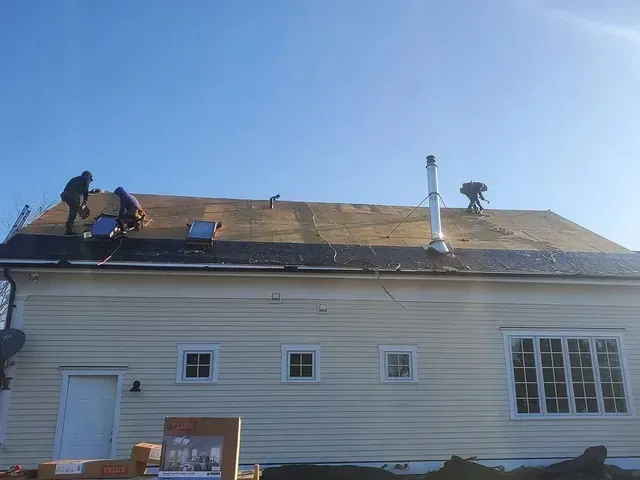 Roofers working on a residential roof under a clear blue sky.