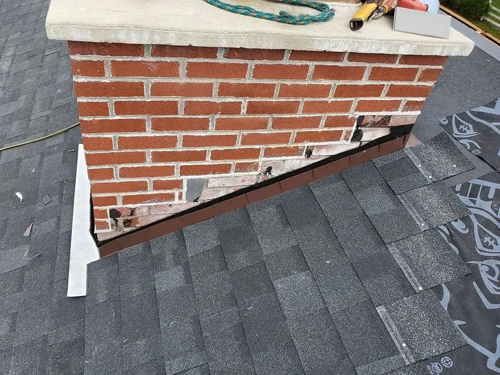 Brick chimney with missing bricks, flashing, and roofing shingles.