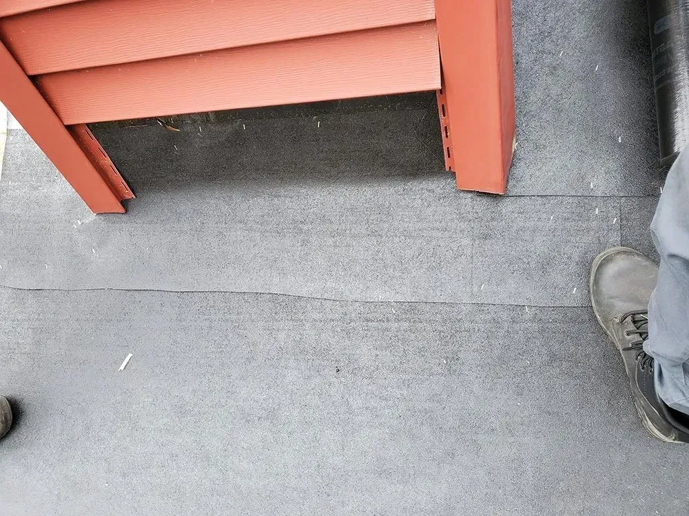 Red siding and trim over gray ground cover. A person's shoe is visible at the edge.