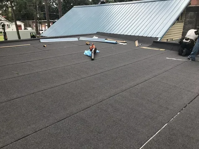 Flat roof with asphalt shingles being installed; workers are present.