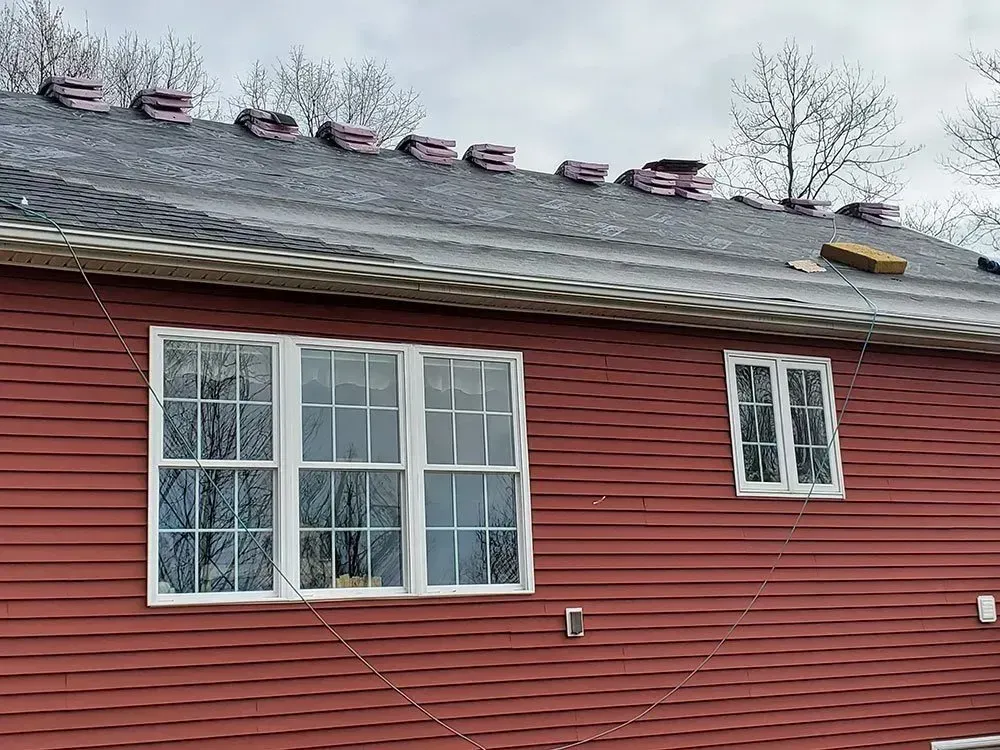 Red house with open windows. Gray roof has shingles lined up. Safety lines are visible.