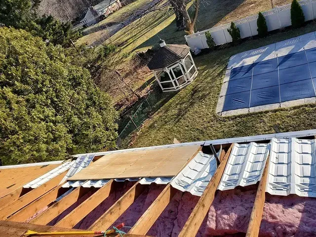 Roof with damaged sheathing, view of a yard with a gazebo, pool, and trees.