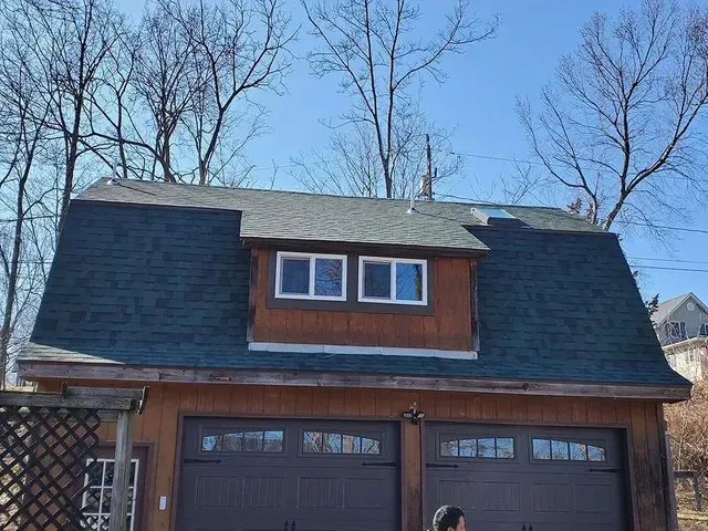 Brown garage with green roof and dormer window, under blue sky.