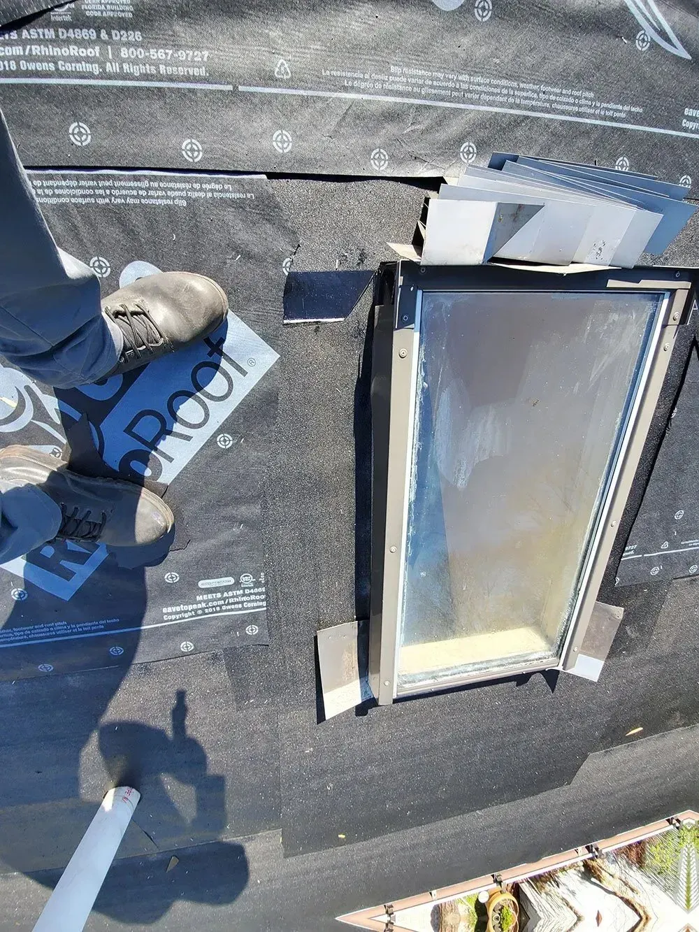 Person installing flashing around a skylight on a black roof.