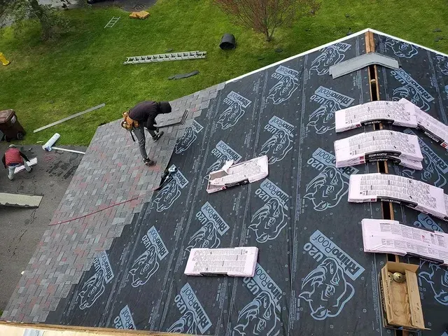 Roofer installing shingles on a roof. The roof is partially covered with underlayment.