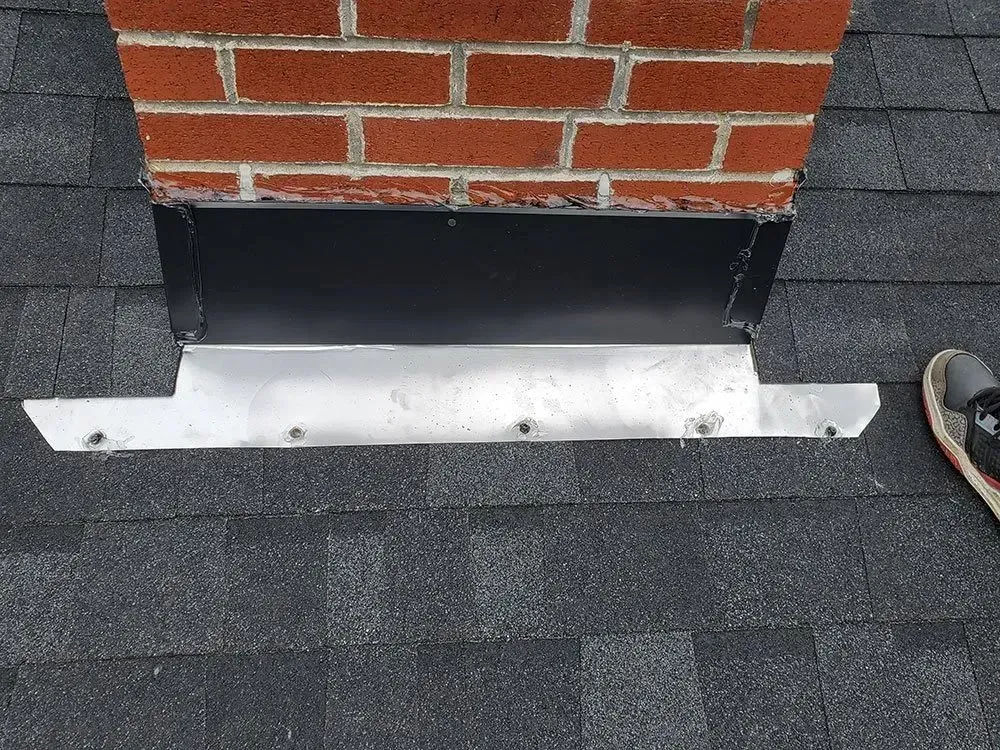 Brick chimney with black and silver flashing on a shingled roof.