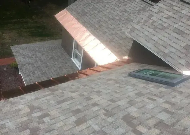 Copper flashing and gutters on a gray shingled roof with a skylight and a small window.