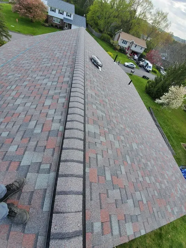 A roof with asphalt shingles in shades of gray, red, and brown. A person stands on the roof.
