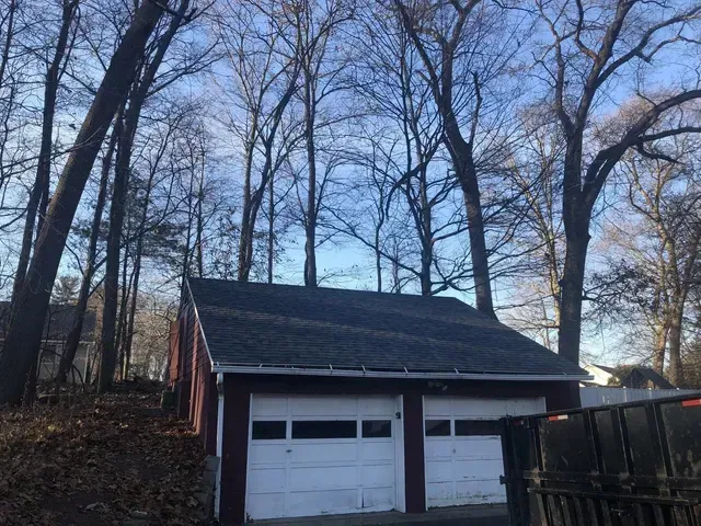 Red garage with two white garage doors, trees in the background, daytime.