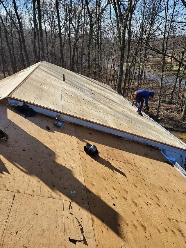 Roofer working on a wooden roof with a forest backdrop on a sunny day.
