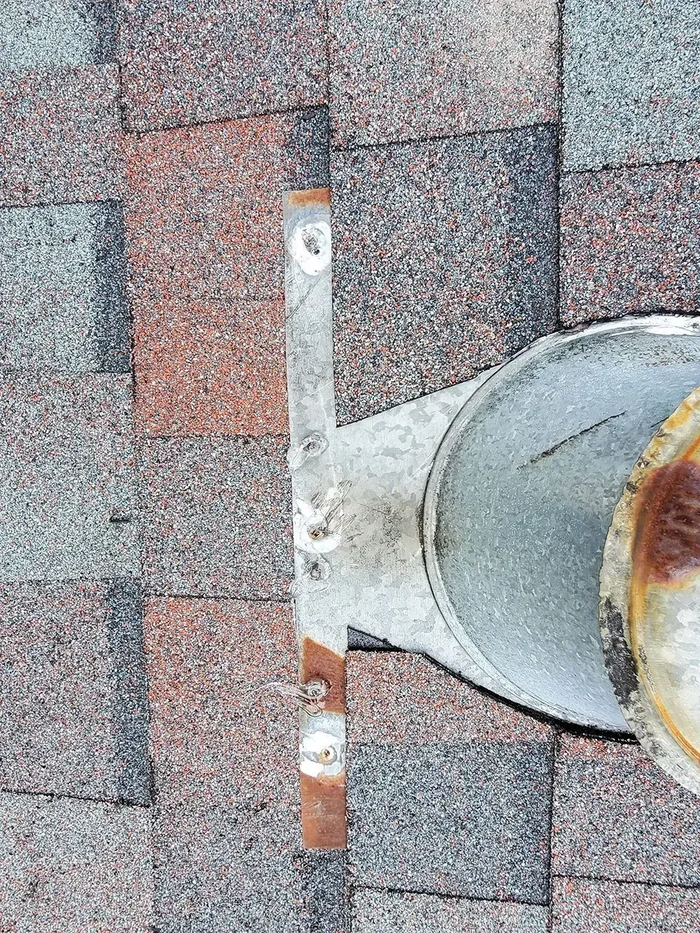 Roof vent pipe with a rusty metal collar on a shingled roof.