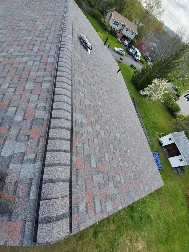 Close-up of a new asphalt shingle roof, gray with red accents. Edges have a darker gray, decorative trim.