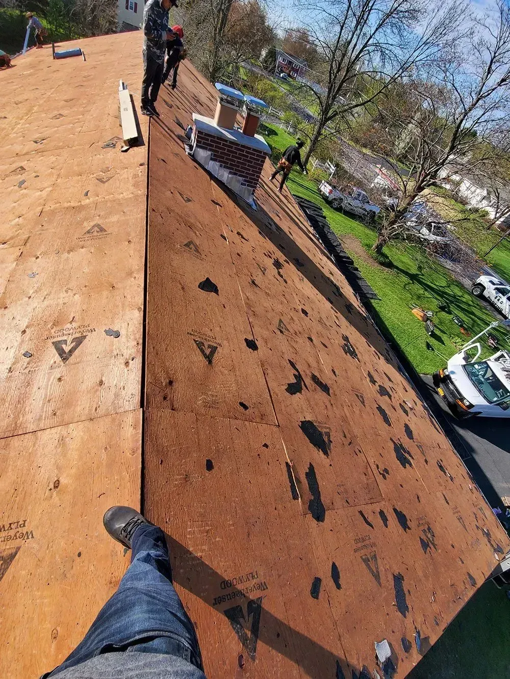 Person on a roof working near a chimney, with asphalt shingles.