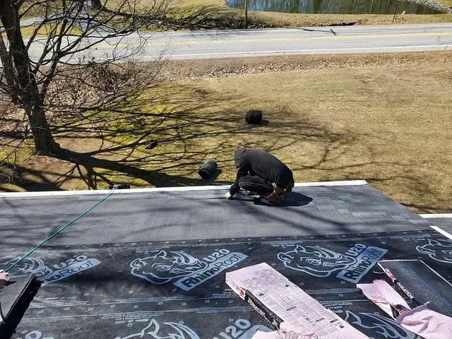 Person on rooftop installing roofing material on a sunny day.