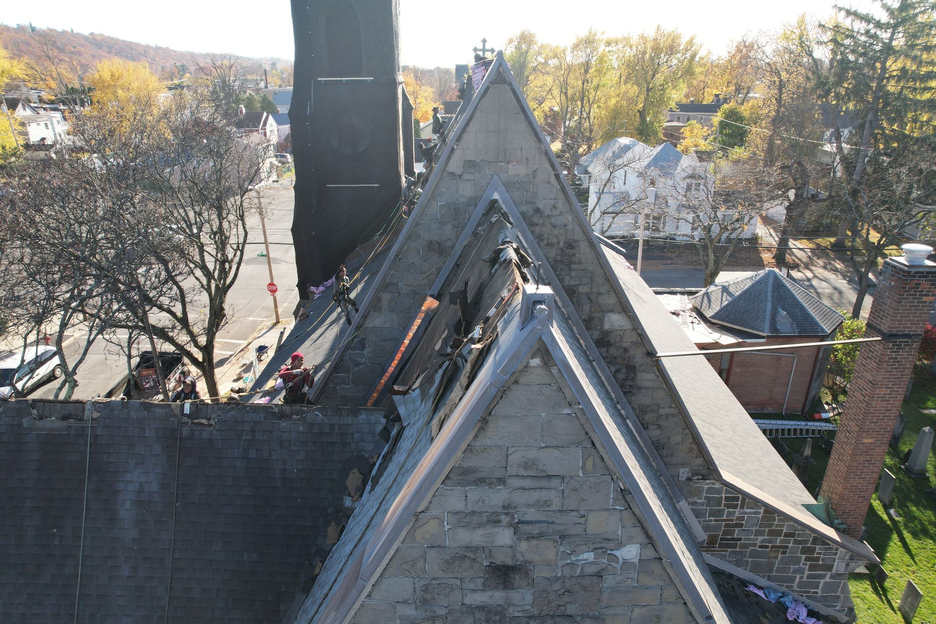 Overhead view of church roof with workers, trees in autumn, and street.