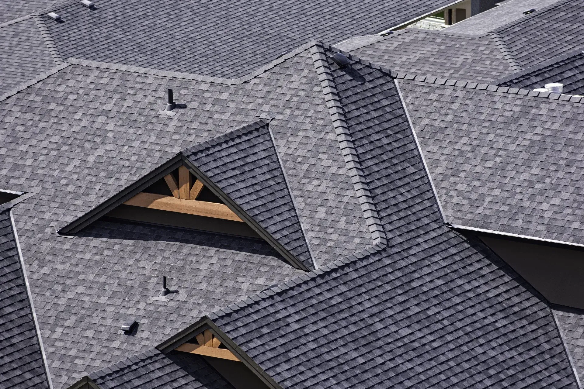 Dark gray asphalt shingle roofs of a house. Triangular roof with wooden beams is visible.