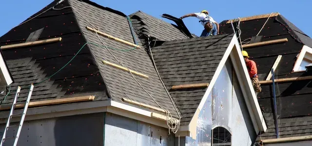 Roofers working on a house roof. Blue sky in the background.