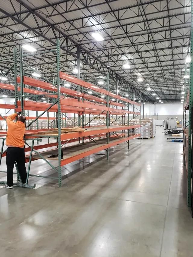 A man is standing next to a row of shelves in a large warehouse.
