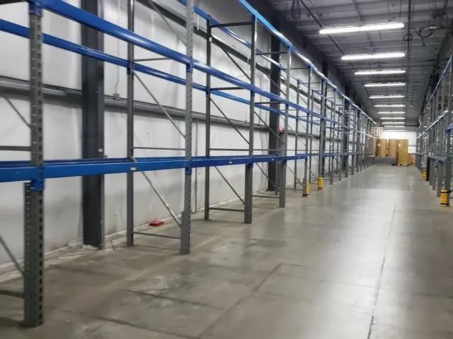 An empty warehouse with blue shelves and a concrete floor