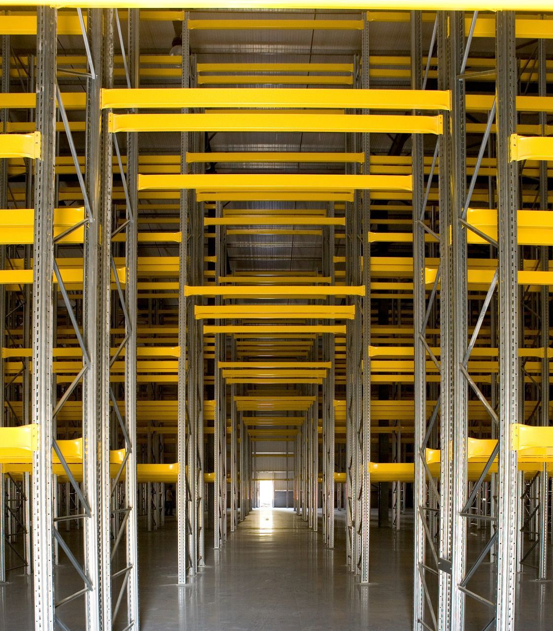 A warehouse with lots of yellow shelves and a light at the end