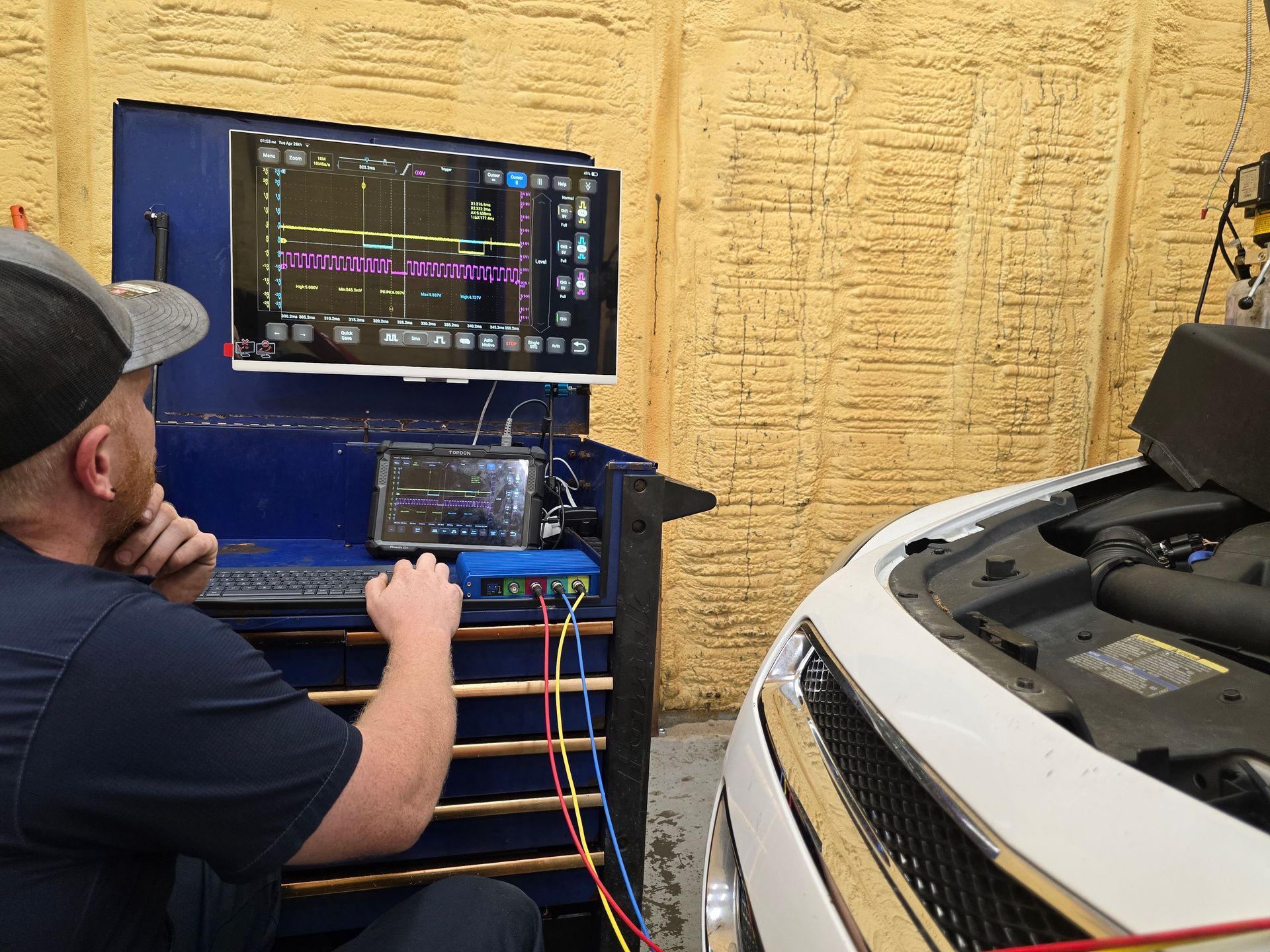 Technician tuning a car with diagnostic monitors beside an open hood in a garage | Lyons Precision Auto Care