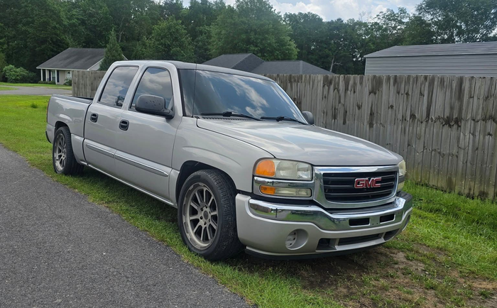 Silver pickup truck parked on a grassy roadside beside a wooden fence | Lyons Precision Auto Care