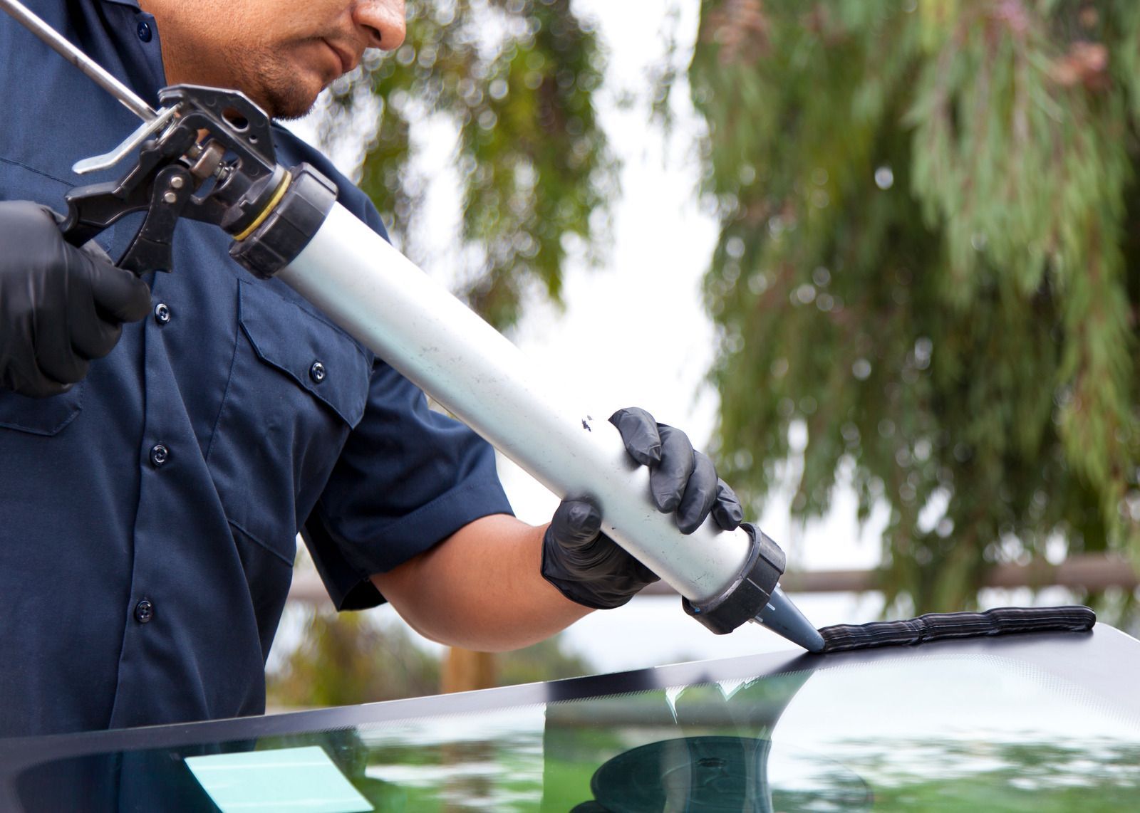 A man is applying sealant to a windshield of a car.