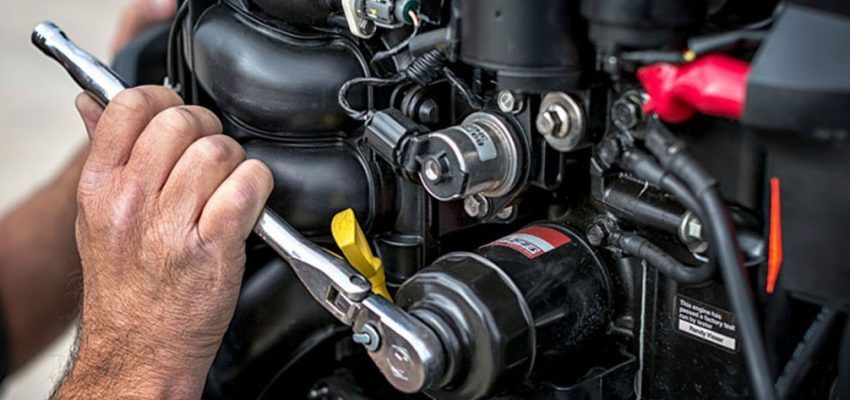 A mechanic using a wrench to work on a black engine. Close up of hands holding a ratchet.