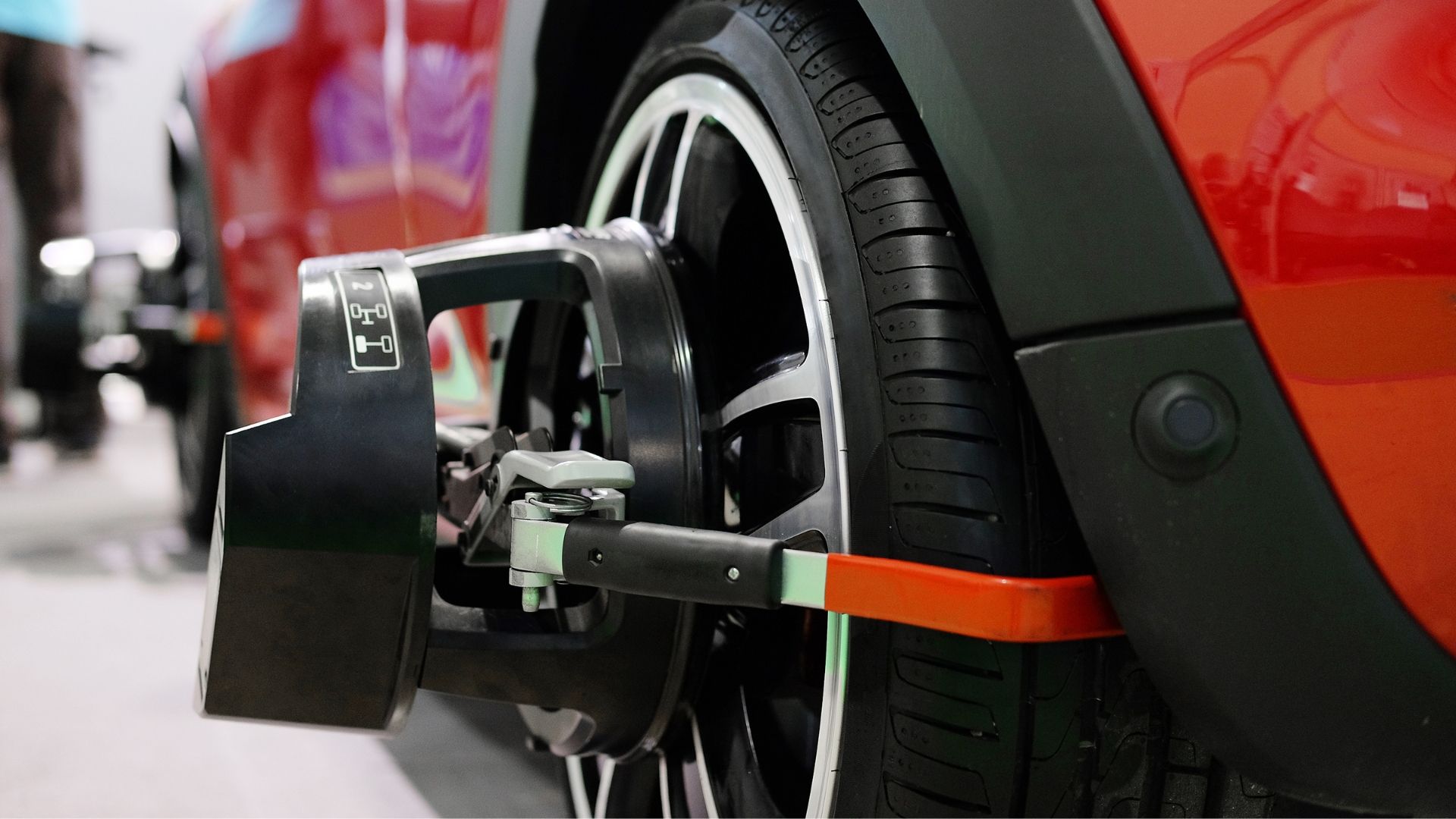 Car wheel with alignment equipment attached; red car in shop.