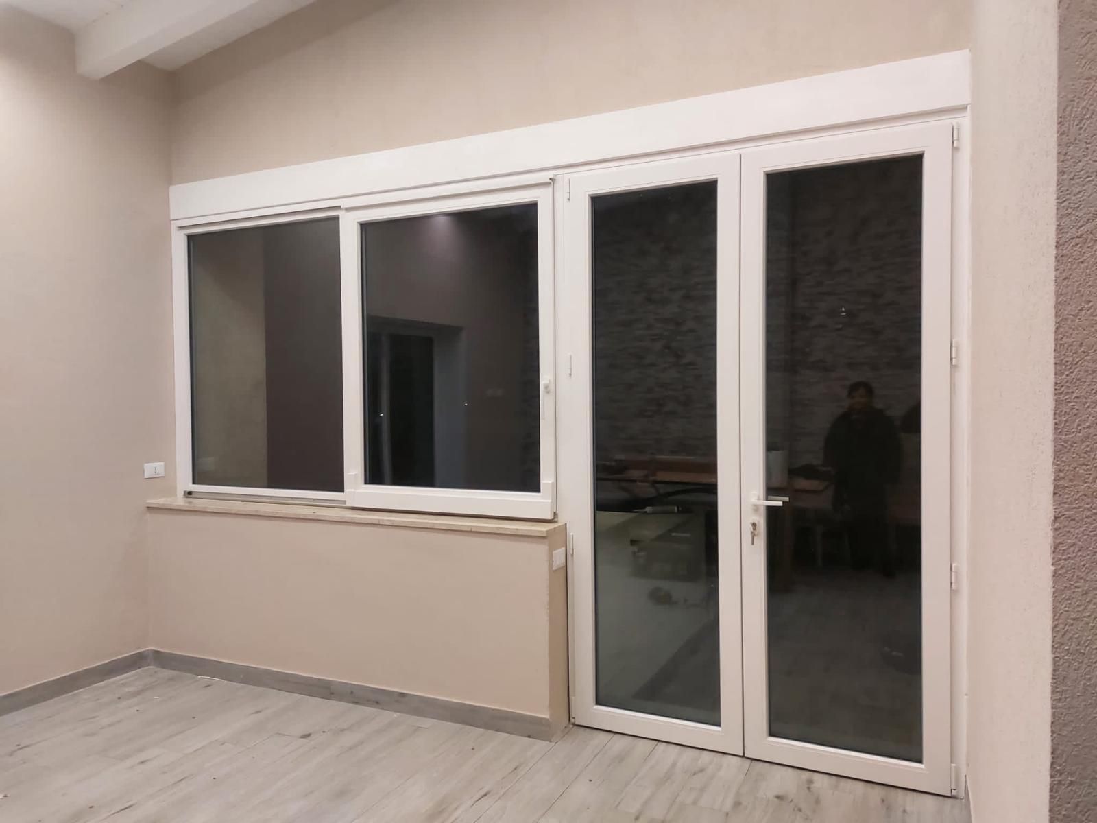Uomo in tuta blu che installa il telaio di una finestra, in un interno.