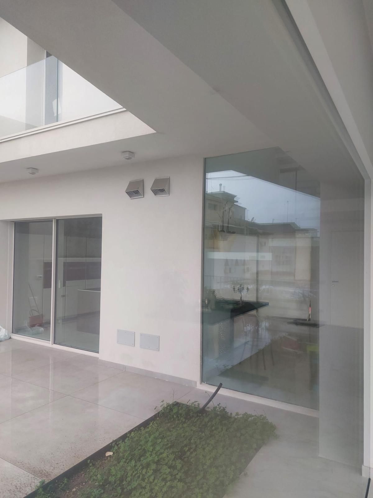 Veranda coperta con sedie, porta e finestre. Rivestimento e finiture grigio chiaro, porta in legno.