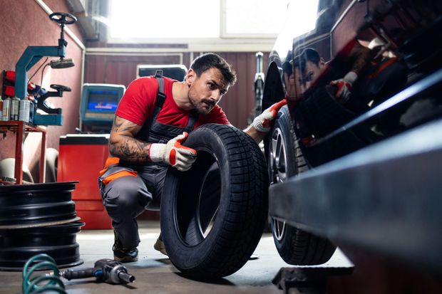 Mechanic in red shirt fitting a tire onto a car wheel in an auto shop