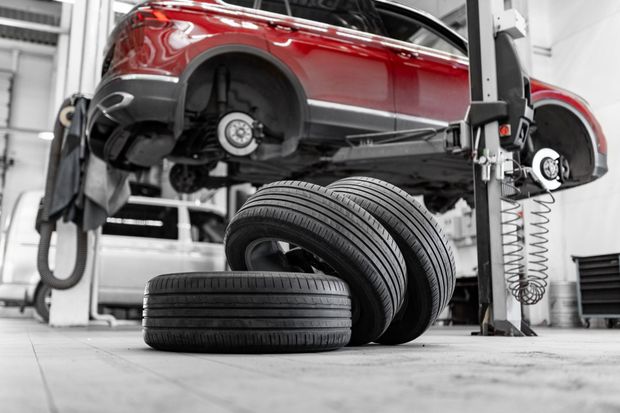 Red car lifted in auto shop with tires stacked underneath and one wheel removed