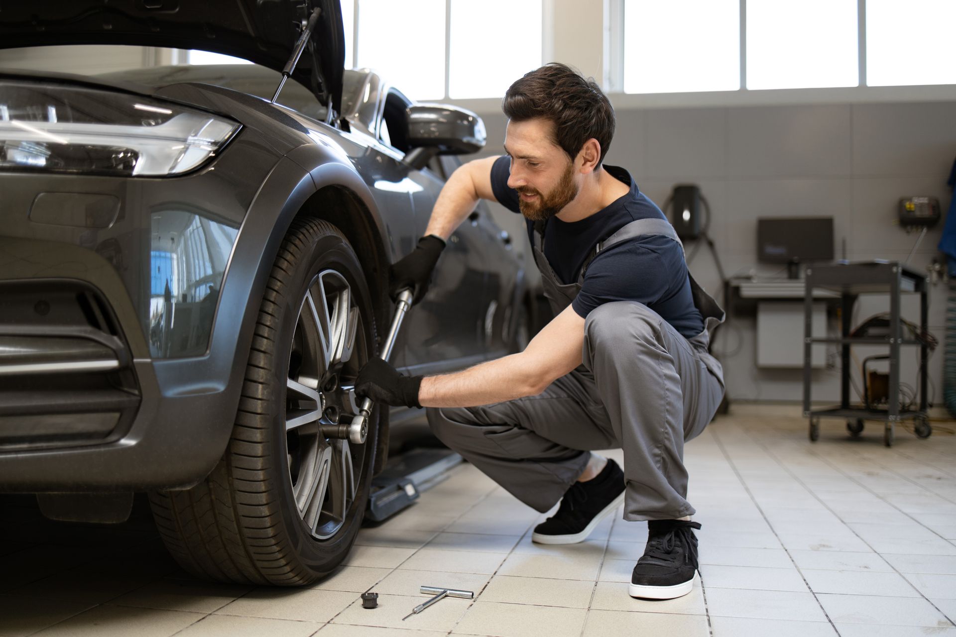 Mechanic crouching beside a black car, checking the front wheel in a garage