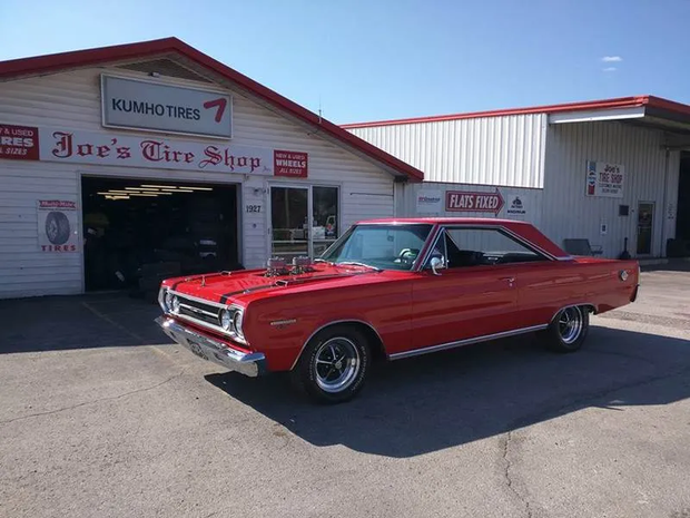 Red classic convertible parked outside Joe’s Tire Shop under a KUMHO TIRES sign.