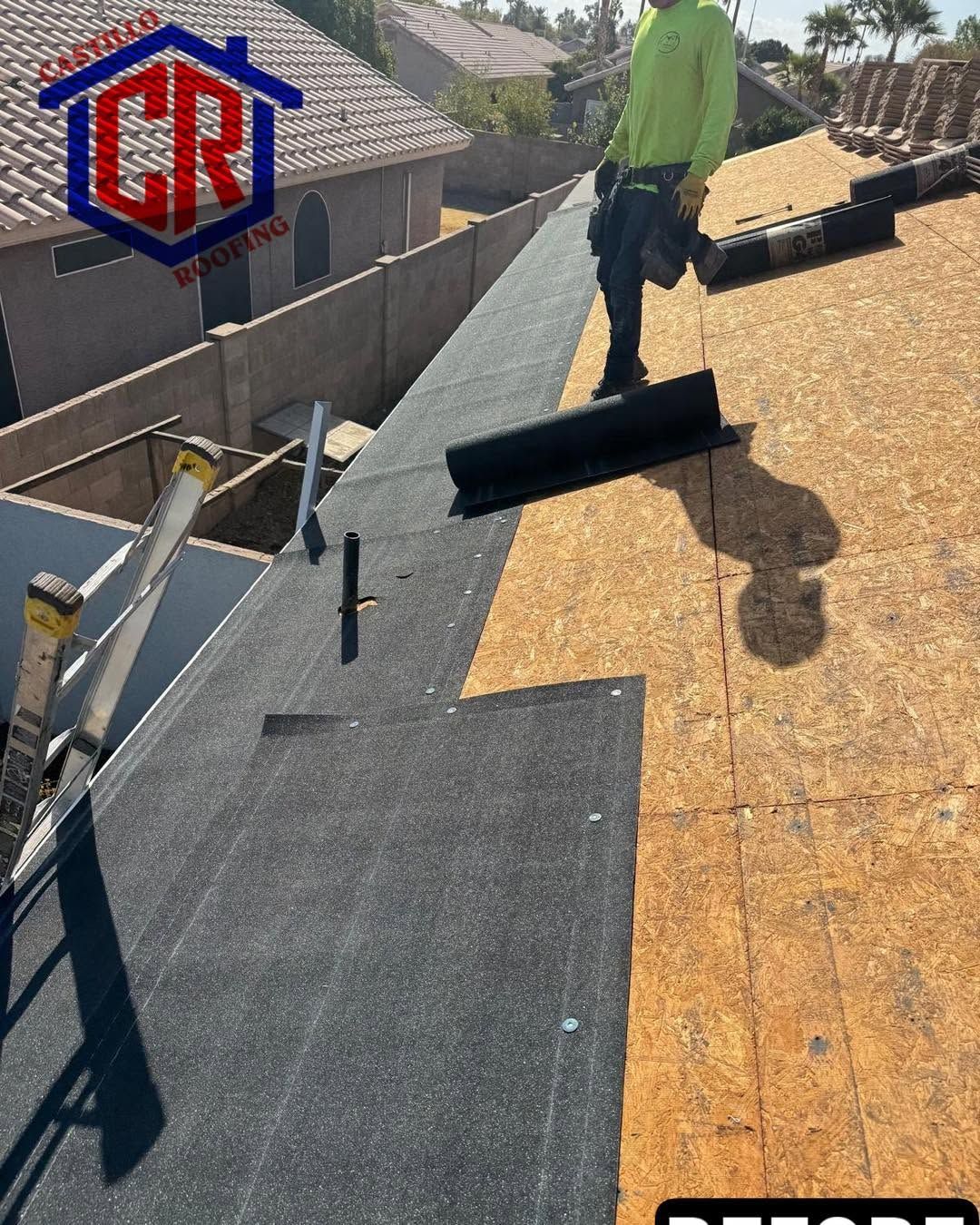 Worker installing roofing underlayment on a sloped roof with gray and tan materials.