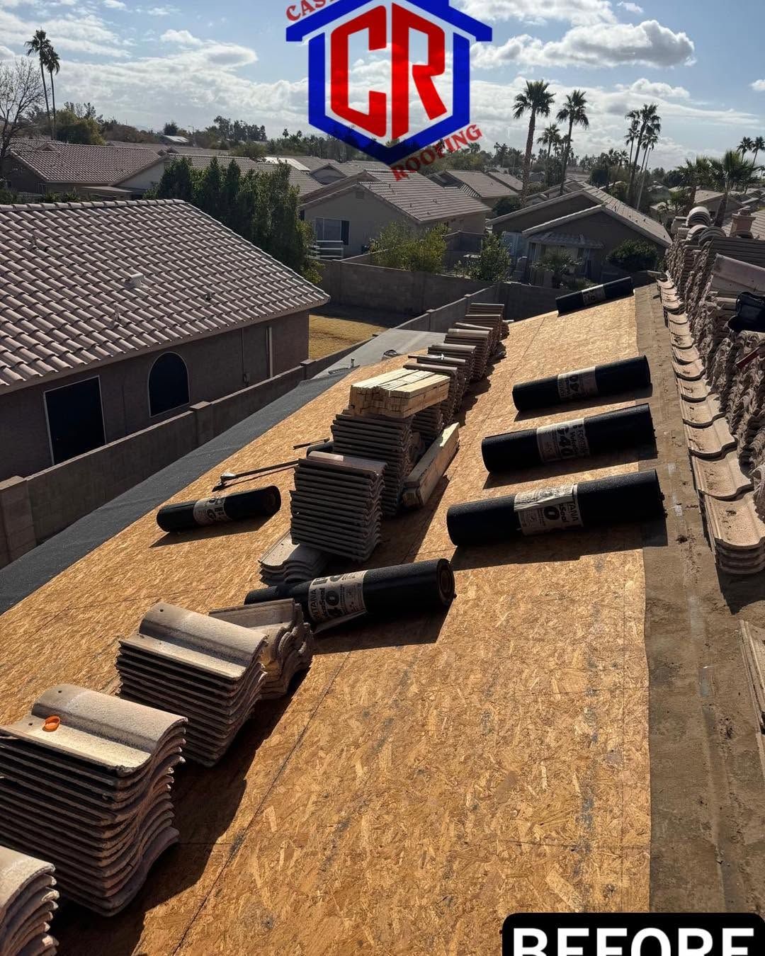 Roof underlayment materials staged on a rooftop, with stacks of shingles and black bundles along the ridge.