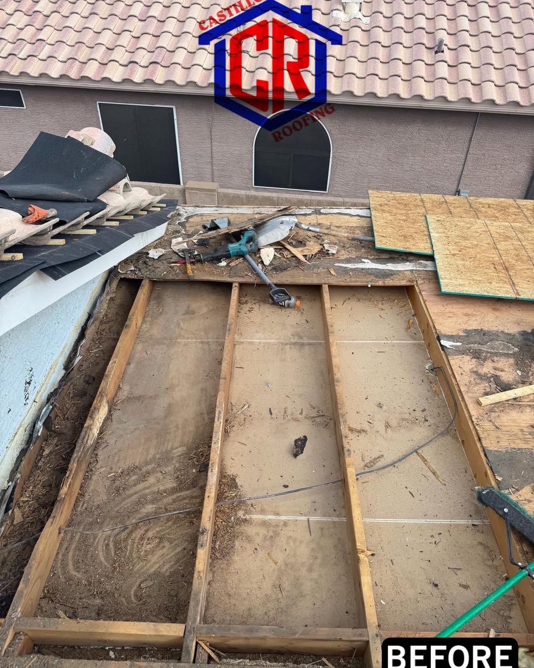 Roof under repair with exposed wooden framing, torn shingles, and debris beside a house.
