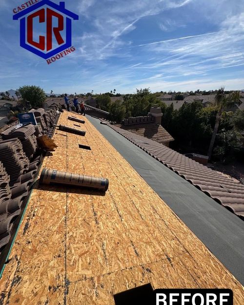 Roof under construction with plywood decking, rolled roofing, and workers on a sunny rooftop.