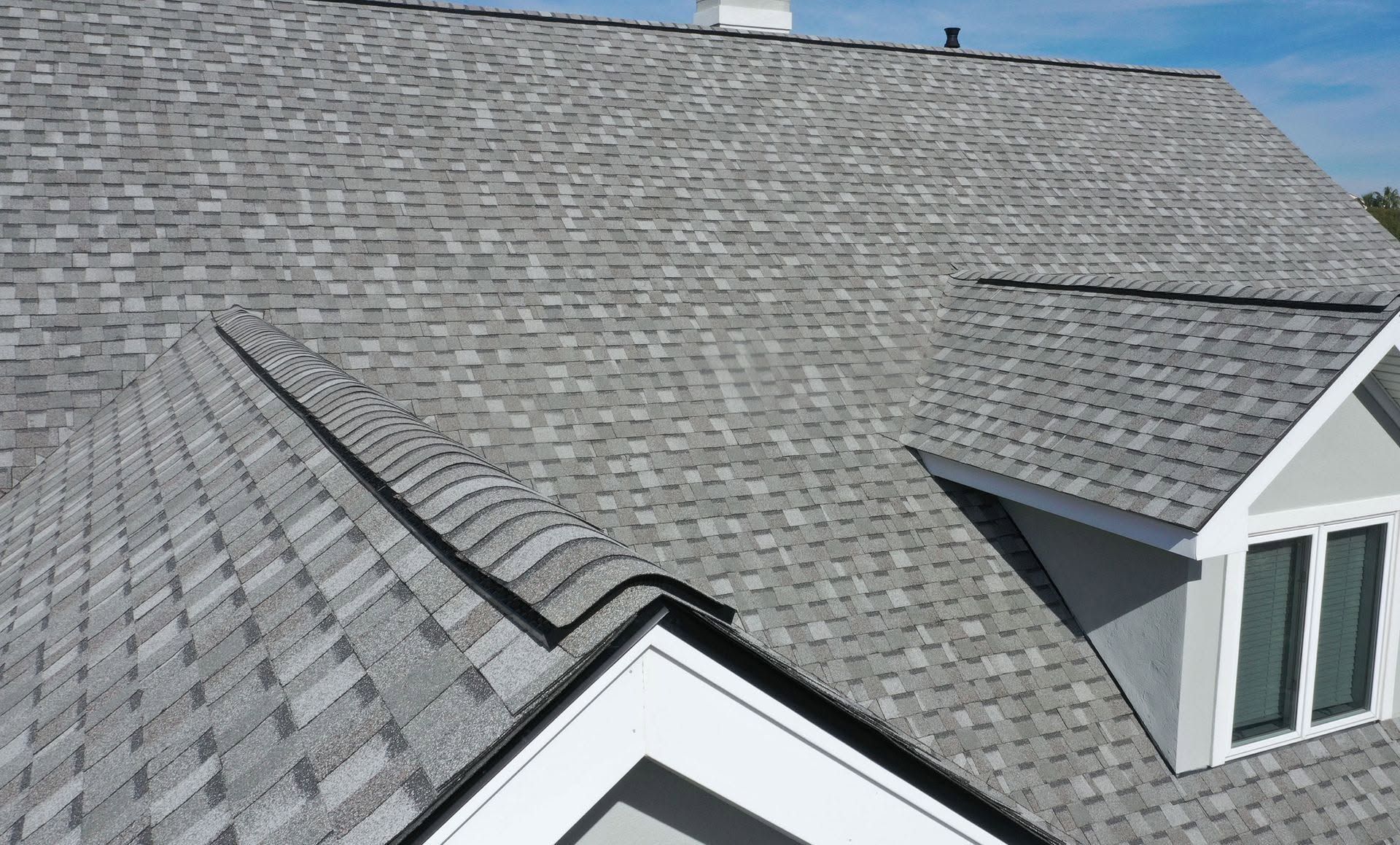 Gray shingled residential roof with dormers and skylights under clear daylight