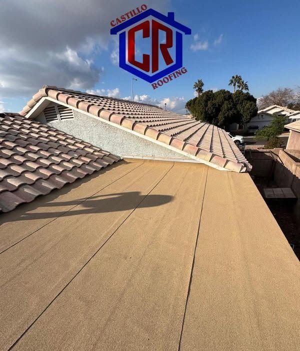 Roof with tan underlayment beside completed gray tile roofing under a blue sky