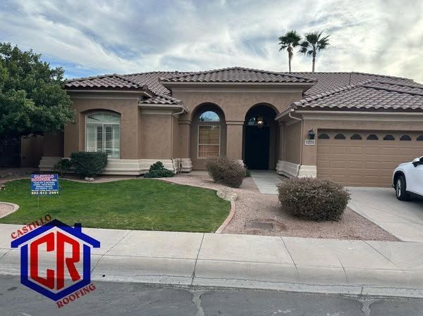 Single-story tan stucco house with a tiled roof, front lawn, driveway, and arched entryway