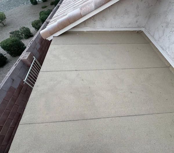 Rooftop patio with beige surface, brick wall, and white railing beside a sloped roof edge